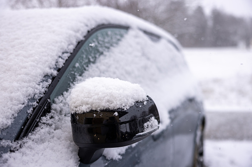 Close up of a car with side view mirror fully covered in snow during winter