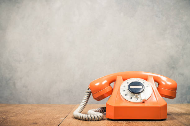 Retro outdated orange rotary telephone from 60s on wooden desk front textured concrete wall background. Vintage old style filtered photo stock photo