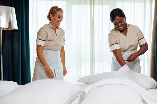 Interracial young hotel maids in white uniforms laughing while working together