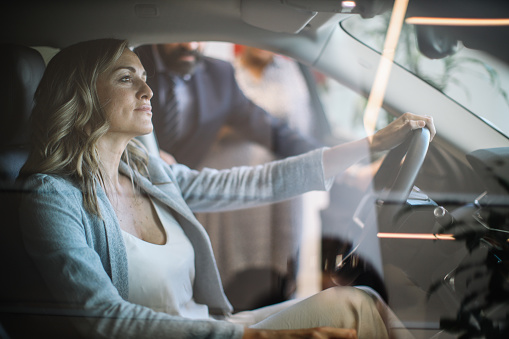 Mid aged woman visits the car dealership, looking at the current offers, talking to the salesperson. Thinking of going EV or staying with the internal combustion car.
