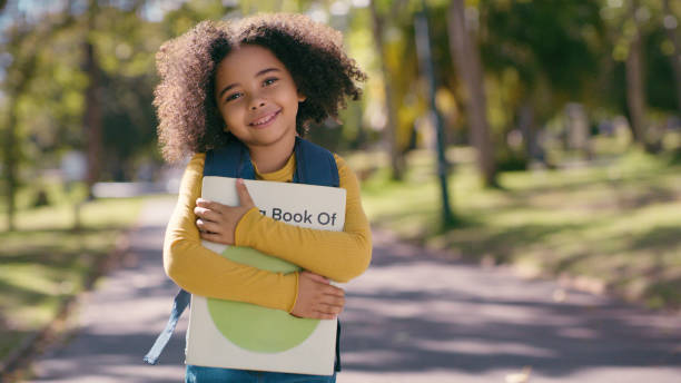 retrato, educação e uma menina no parque com um livro para estudo, aprendizagem ou desenvolvimento infantil. crianças, escola e uma jovem estudante em pé ao ar livre em um jardim para crescimento futuro ou conhecimento - africa child reading african descent - fotografias e filmes do acervo