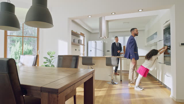 Male real estate agent showing the kitchen in a modern home to a man with a small daughter