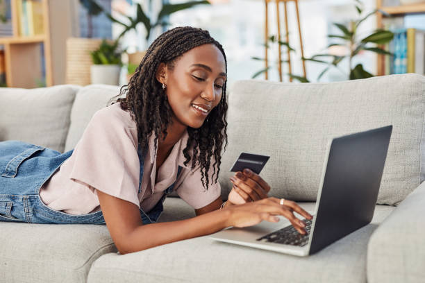 Online shopping, woman with laptop and credit card for payment on a sofa in living room of her home. Ecommerce, investment or pay bills and African female person with bank information for internet stock photo