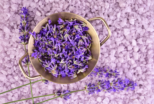 Fresh lavender flowers in an iron bowl on a background of lavender bath salts. Flat lay.