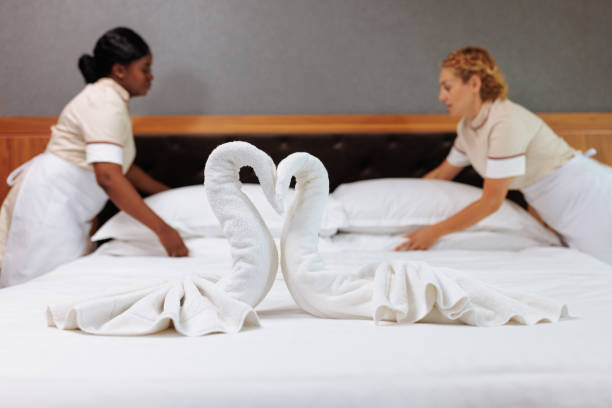 Two young uniformed interracial hotel maids finishing bedding