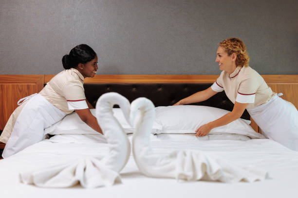 Swan shaped decoration on the bed and two uniformed interracial hotel maids in the background