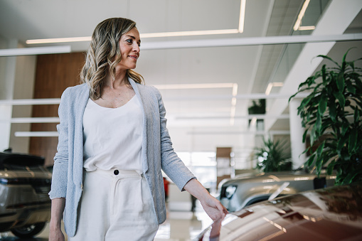 Mid aged woman visits the car dealership, looking at the current offers, talking to the salesperson. Thinking of going EV or staying with the internal combustion car.