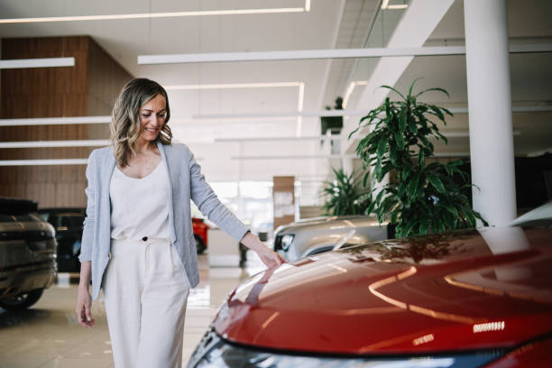 confident mid age woman looking out for the new car Mid aged woman visits the car dealership, looking at the current offers, talking to the salesperson. Thinking of going EV or staying with the internal combustion car. bmw dealership stock pictures, royalty-free photos & images