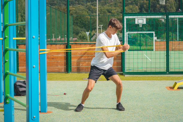 un adolescent axé sur les objectifs travaillant sur son corps à l’aide de caoutchouc de résistance effectue un entraînement en force. préparation de la saison sportive. faire de l’exercice avec votre propre corps. aire de jeux d’entraînement en - male torso abdominal muscle the human body photos et images de collection