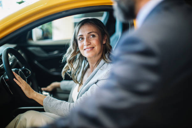 businesswoman looking for a new car Mid aged woman visits the car dealership, looking at the current offers, talking to the salesperson. Thinking of going EV or staying with the internal combustion car. bmw dealership stock pictures, royalty-free photos & images