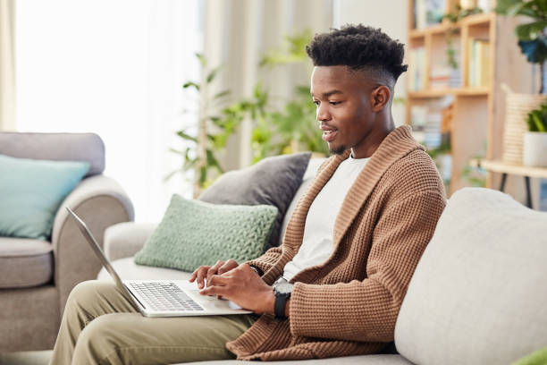 istock Laptop, remote work and internet, black man on sofa in lounge, checking email or research for freelance job at home. Communication, technology and training online, young African agent working on web. 1502313149