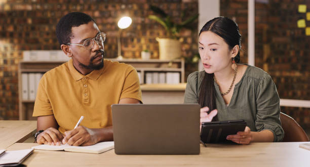 istock Training, talking and business people with technology at night or planning a deadline. Teamwork, late and a black man and woman with notes and conversation about a writing project on tech in office 1502314605