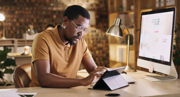 istock Black man in office, late night and scroll on tablet at design agency, planning online schedule for deadline. Overtime, project manager or designer in digital marketing, reading email or social media 1502315251