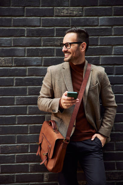 istock A smiling businessman is holding a mobile phone and leaning on a brick wall. 1502323344