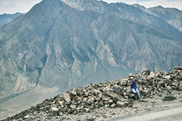 istock Female backpacker is having a rest sitting on rock heap next to high mountain road 1502334155