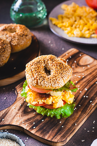 Hearty bagel burger with scramble egg, bacon, cheese, tomato and lettuce vertical view