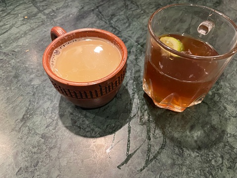 A cup of traditional brewed milk tea in a clay cup next to a cup of lemon tea.