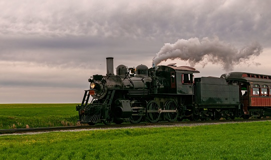 A restored steam passenger train traveling by on a cloudy day.
