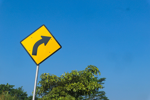 Black arrow traffic sign on yellow background on the bright sky background