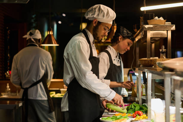 istock Young multiethnic male chef peeling fresh zucchini while standing by workplace 1502384653