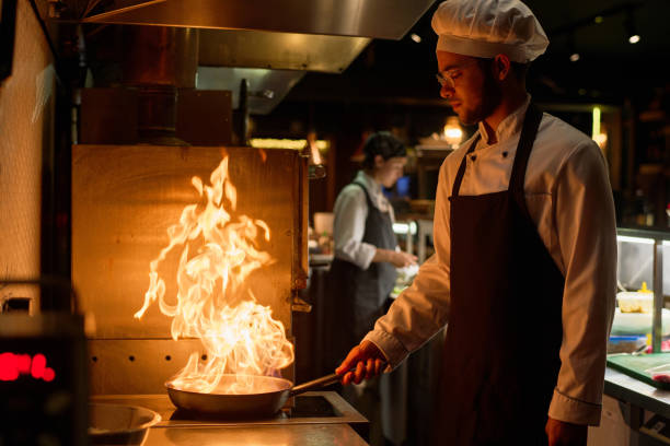 istock Young chef in uniform preparing new dish in frying pan with burning fire 1502384669