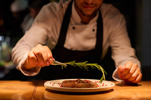 bàn tay nam đầu bếp trẻ đặt thảo mộc thơm lên trên thịt nướng - fine dining hình ảnh sẵn có, bức ảnh & hình ảnh trả phí bản quyền một lần