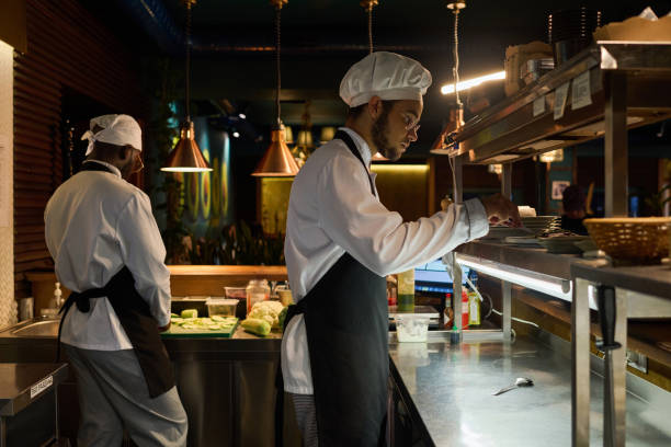 istock Side view of young male chef in uniform preparing dish for serving 1502384754