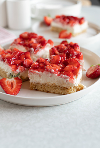 Fresh and homemade baked strawberry cream cake with mascarpone. Served slice and in pieces on a platter on white table background. Closeup with copy space.