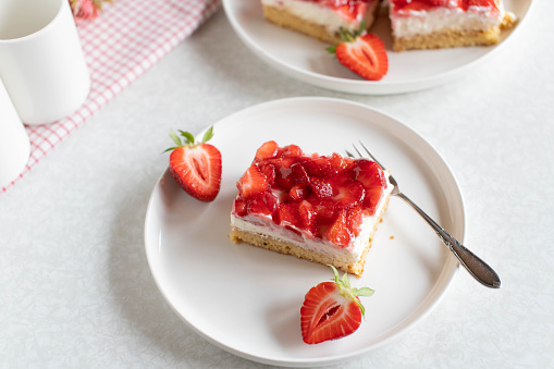 Fresh and homemade baked strawberry cream cake on short crust pastry. Served on a white plate with decoration on light table background from above.