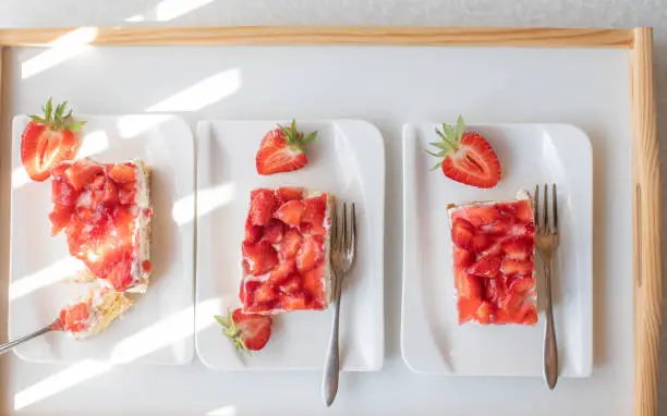Delicious summer dessert with a homemade strawberry cream cake. Baked as a sheet cake. Served sliced on white plates with fork isolated on white background. Top view