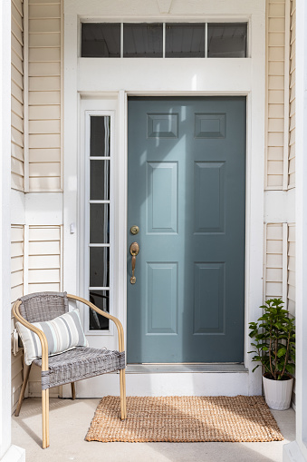 A cozy front door and small front porch with a blue door, tan siding, and a chair and plant as decorations.