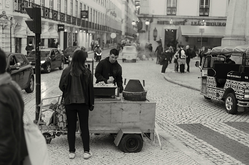 Lisbon, Portugal - Mars 11, 2023: A traditional roasted chestnuts vendor attends a client in a street in Lisbon downtown.
