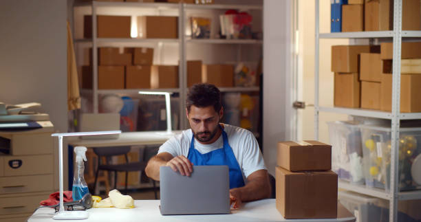 istock Male hacker in janitor uniform steal information on laptop in modern warehouse 1502390787