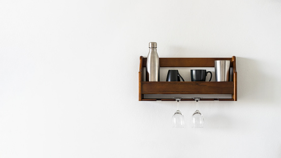 A shelf with mugs and glasses in the kitchen on a blank white wall. Storage of kitchen utensils and glasses. Copy space panoramic header