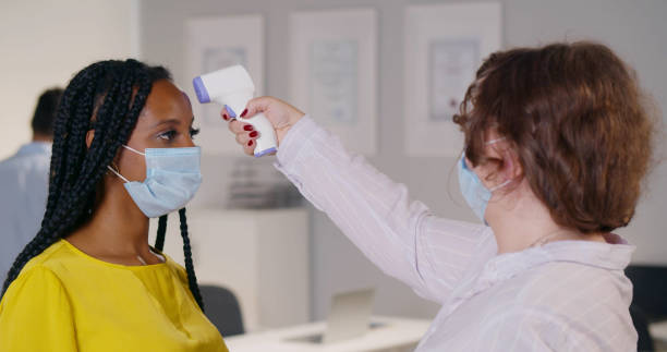les employés de bureau portant un masque de sécurité ont vérifié avec un thermomètre sans contact pendant la pandémie de coronavirus. - infrared thermometer photos et images de collection