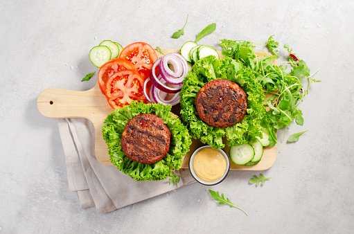 Freshly Grilled Burger Patties, Plant Based Meatless Burgers with Fresh Lettuce and Vegetables on a Wooden Board on Bright Background