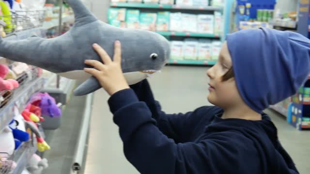 A cute boy takes a toy shark in a toy store and examines it i