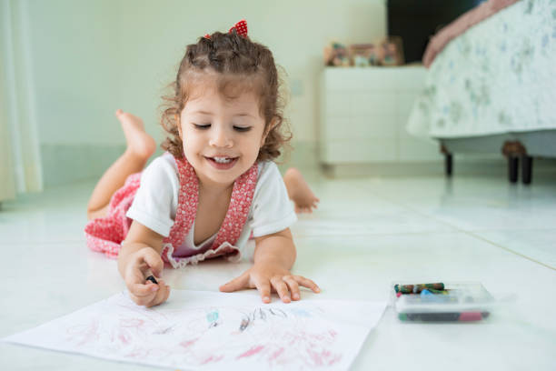 Happy child lying on the bedroom floor drawing using colored pencils