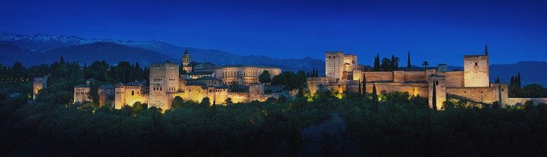 Panoramic view of Alhambra at night with Sierra Nevada Mountains on background - Granada, Andalusia, Spain