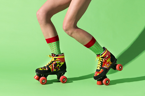 Side view of anonymous young female legs in colorful socks riding light and robust adjustable roller skates with shadow on lime color skating rink