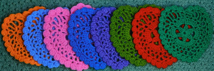 Several multicolored crocheted woolen threads decorative napkins in the shape of hearts on a green background. Top view, web banner. Close-up, slight blur and fuzziness.