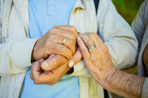 Close up of elderly couple holding hands while walking in the nature. Husband and wife holding hands and comforting each other. Love and care concept.