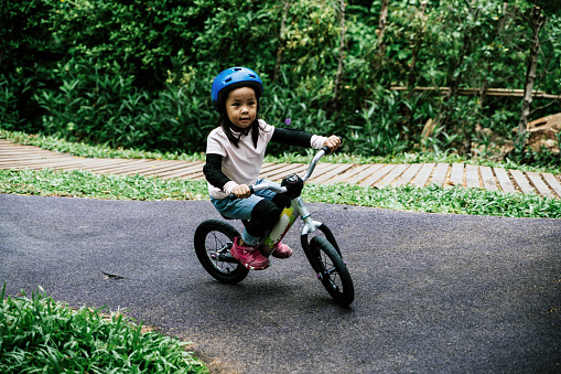 Little girl with helmets practicing balance bike in public park