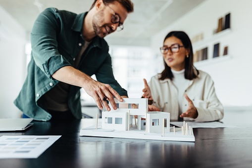 Architects working on a house model in a creative office. Two young business people having a discussion on a new design project.