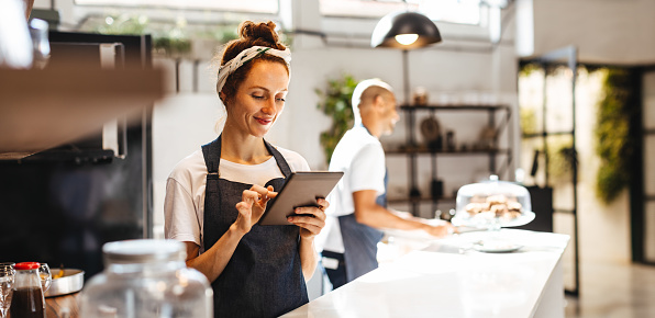 Cafe waitress using a digital tablet to manage orders. Woman using a touchscreen device that helps her to view and organize orders effectively, ensuring prompt and efficient service for the customers.