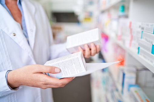 Pharmacists standing in front of medicine shelves and holding medicines and prescription. Close up of hands, unrecognizable person.