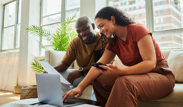 istock A young interracial couple smiles using their laptop computer and mobile phone to work on their budget and finances from home.stock photo, copy space 1502425336