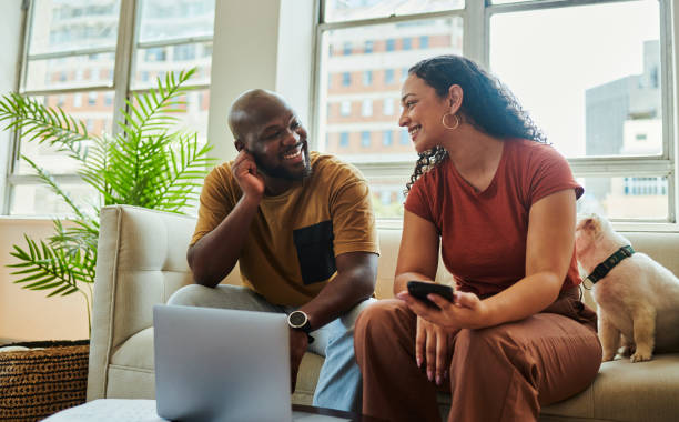 istock A young couple sitting on the couch with a laptop computer looking at each other while smiling. 1502425341