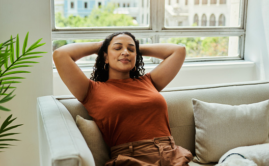 A young woman wearing orange sits relaxed with her eyes closed and hands stretched behind her head, stock photo, copy space