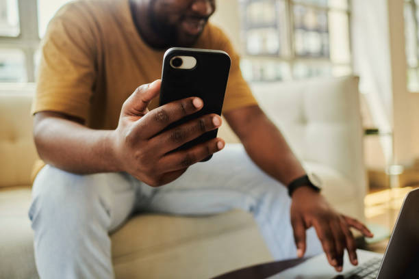 istock A young black man sitting on his sofa  while smiling and texting on a mobile phone and  laptop computer . Stock photo, copy space 1502426054